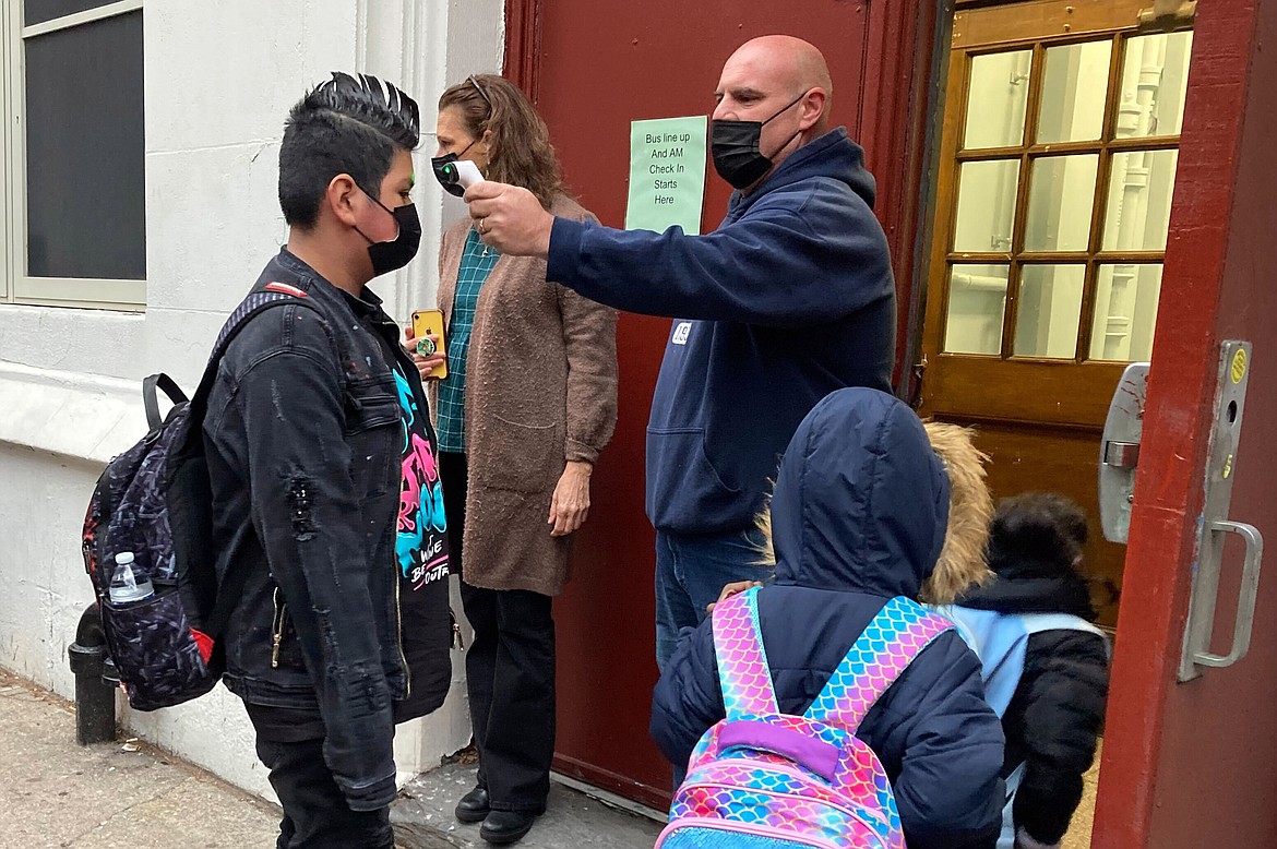 John Marro, the dean of students at P.S. 347, The American Sign Language and English Lower School, in New York, takes students' temperatures as they arrive on the first day after the holiday break, Monday, Jan. 3, 2022. New York City schools reopened Monday after the holiday break despite a surge in coronavirus infections. (AP Photo/Jennifer Peltz)