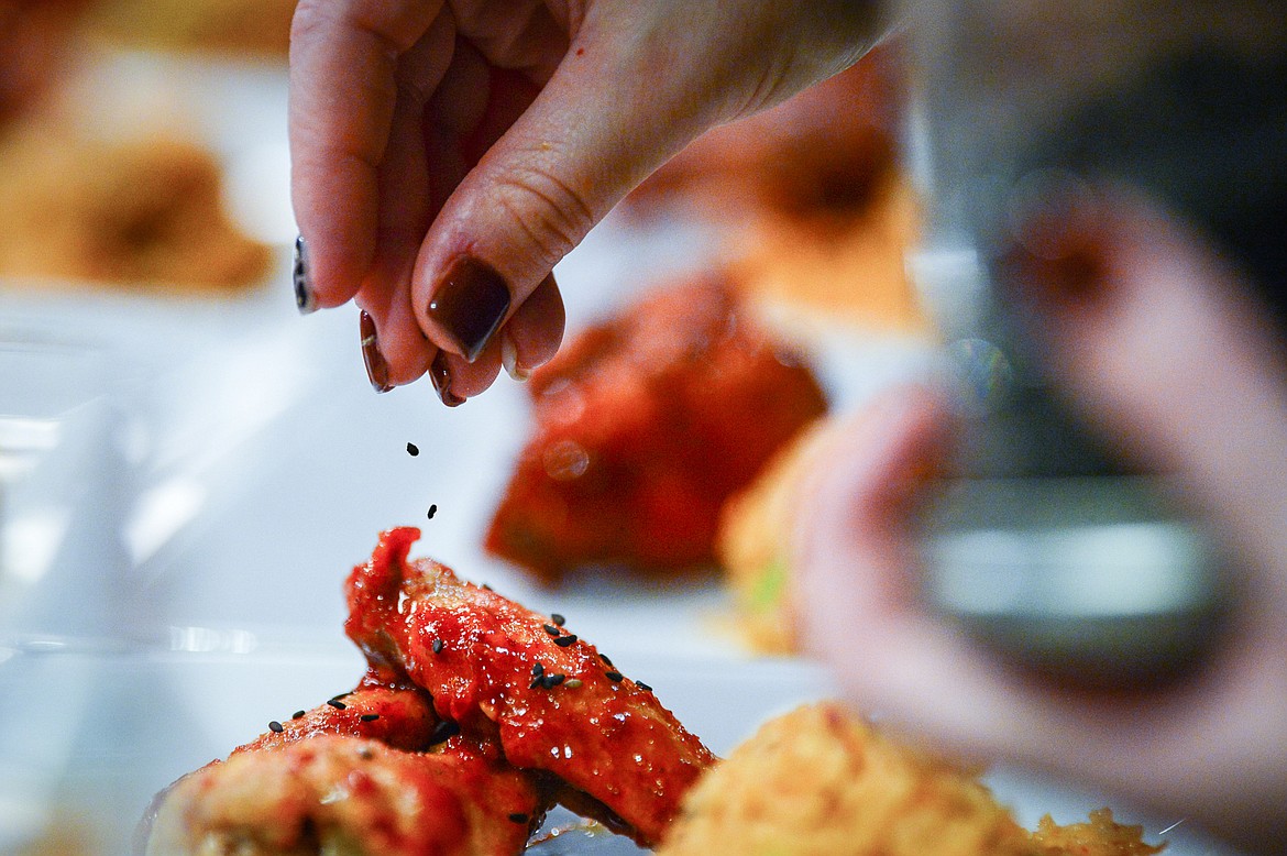 Trovare co-owner Mallory Hickethier sprinkles black sesame seeds on chicken wings for a Kimchi Fried Rice & Korean Chicken Wings dish for attendees of a hands-on cooking class with chef John Evenhuis at Trovare in Whitefish on Tuesday, Jan. 18. (Casey Kreider/Daily Inter Lake)