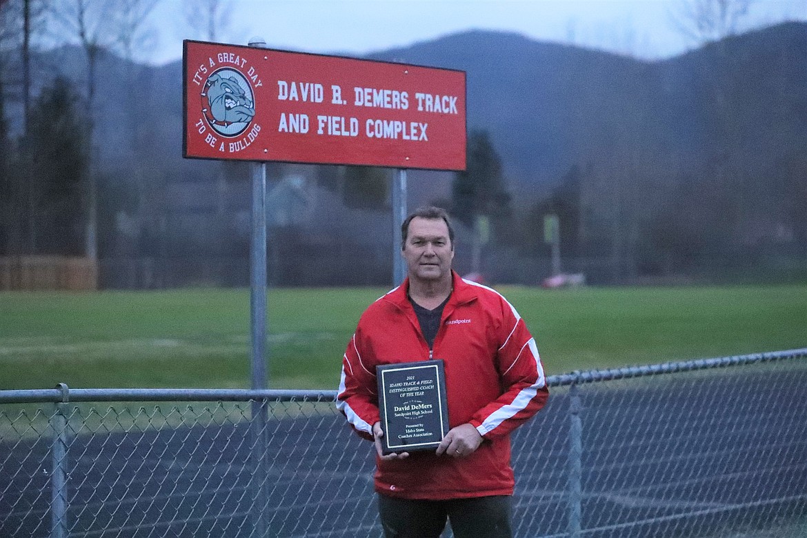 Dave DeMers poses for a photo at the Sandpoint High School track with the 2021 Track and Field Distinguished Coach of the Year Award he recently received from the Idaho State Coaches Association.