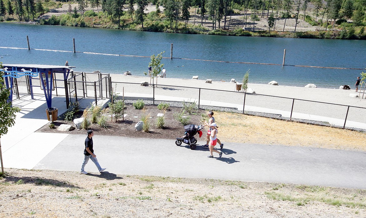 Runners and walkers pass by the dog park on the Spokane River at Atlas Waterfront Park.