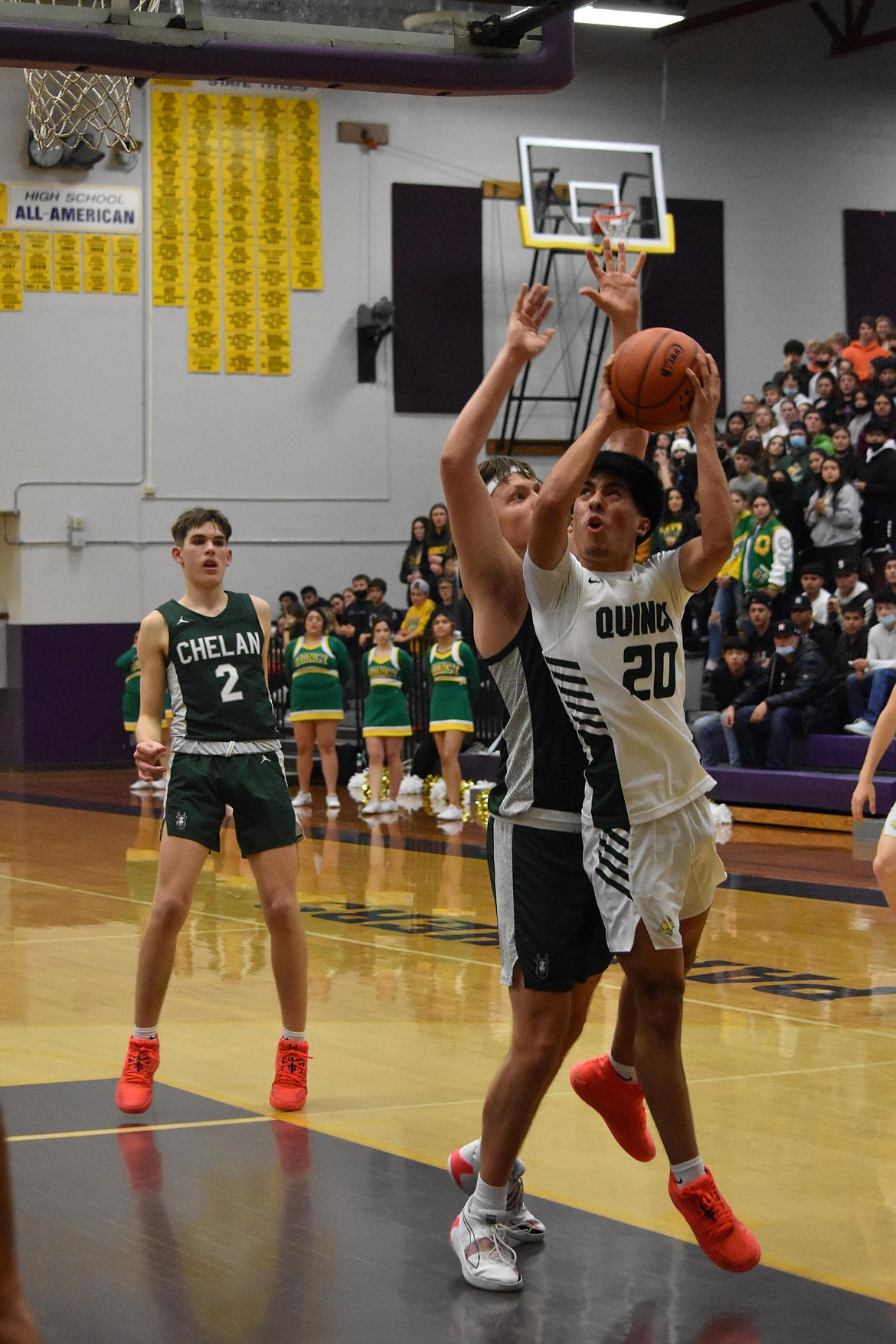 Quincy High School senior Saul Alvarez (20) goes in for a layup as a Chelan High School opponent attempts to block him.