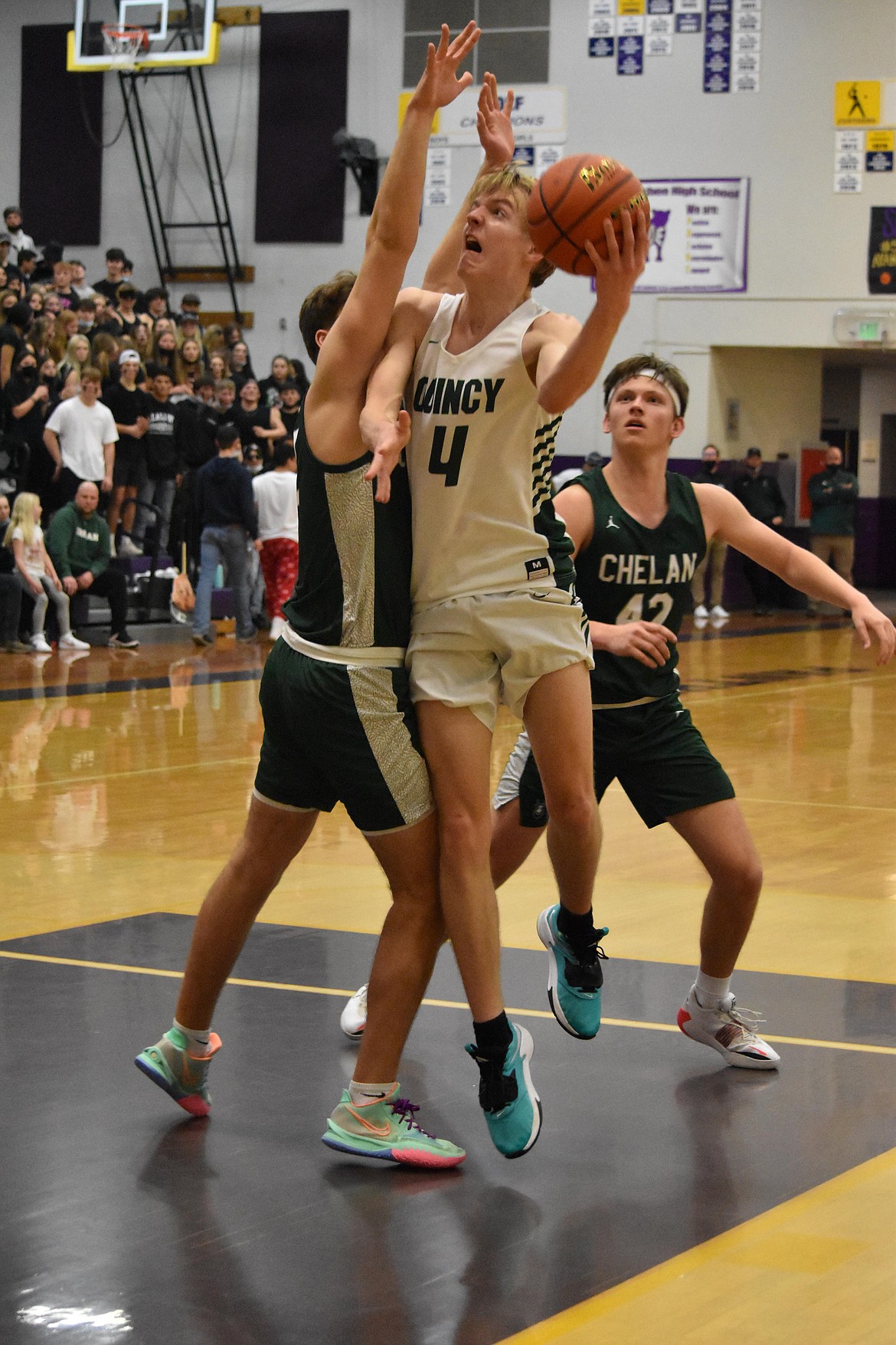 Quincy High School sophomore Aidan Bews (4) goes in for a layup as a Chelan High School opponent attempts to block him.