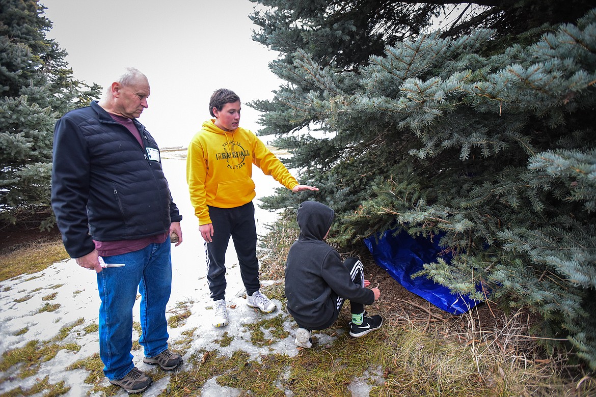 Volunteer Daron Larsen speaks with Boston Johnson and Zander Schmautz while they set up their shelter using a tarp and rope under a pine tree outside Fair-Mont-Egan School on Tuesday, Feb. 15. (Casey Kreider/Daily Inter Lake)