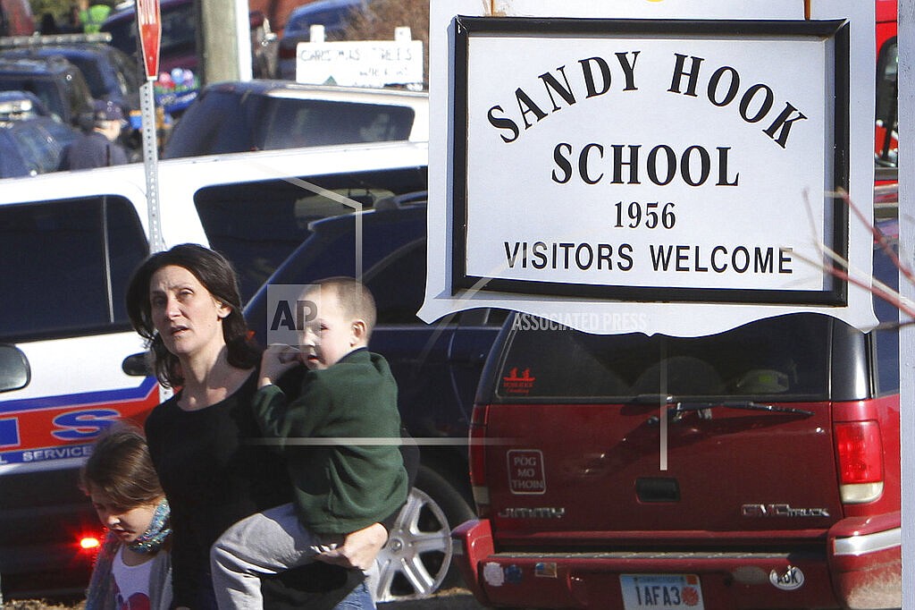 A parent walks away from the Sandy Hook Elementary School with her children following a shooting at the school in Newtown, Conn., Dec. 14, 2012. The families of nine victims of the Sandy Hook Elementary School shooting have agreed to a settlement of a lawsuit against the maker of the rifle used to kill 20 first graders and six educators in 2012, according to a court filing, Tuesday, Feb. 15, 2022. (Frank Becerra Jr./The Journal News via AP)