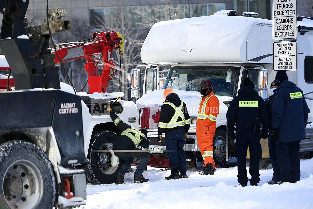 Police officers assist a tow operator to remove a truck from a blockade on Nicholas St. in Ottawa, on Friday, Feb. 18, 2022. Police began arresting protesters Friday in a bid to break the three-week, traffic-snarling siege of Canada's capital by hundreds of truckers angry over the country's COVID-19 restrictions. (Justin Tang /The Canadian Press via AP)