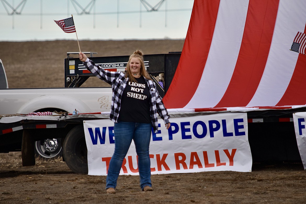 Freedom Ride and Rally organizer Leah Johnson waves a flag in front of an impromptu speakers stage in a bean field west of Moses Lake on Saturday. The ride and rally was organized as a show of support for Canadian truckers who have been protesting vaccine mandates for the last three weeks.