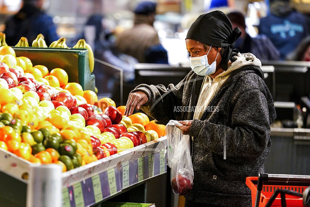 A shopper waring a proactive mask as a precaution against the spread of the coronavirus selects fruit at the Reading Terminal Market in Philadelphia, Wednesday, Feb. 16, 2022. The majority of healthy Americans, including students in schools, can safely take a break from wearing masks under new U.S. guidelines released Friday, Feb. 25. The Centers for Disease Control and Prevention outlined a new set of measures for communities where COVID-19 is easing its grip, with less of a focus on positive test results and more on what’s happening at hospitals. (AP Photo/Matt Rourke)