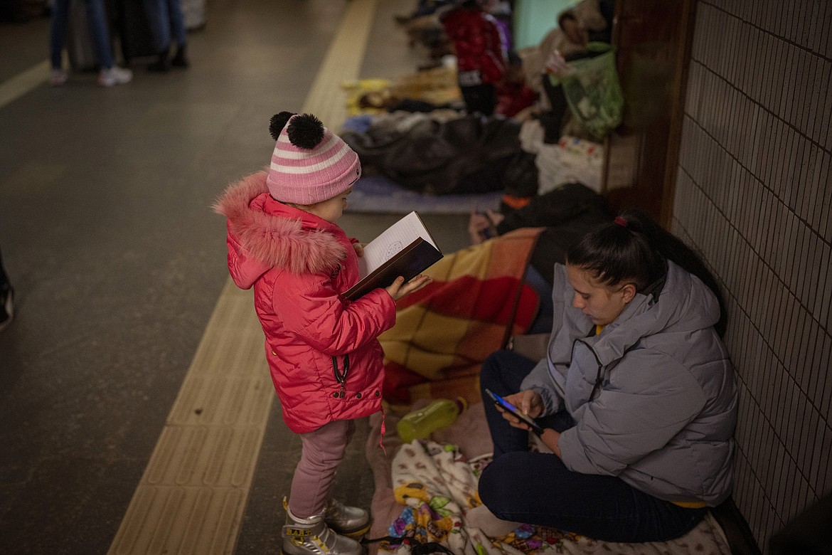 A girl looks at a notebook next to her mother as they stand in the Kyiv subway, using it as a bomb shelter, in Ukraine, Saturday Feb. 26, 2022. (AP Photo/Emilio Morenatti)