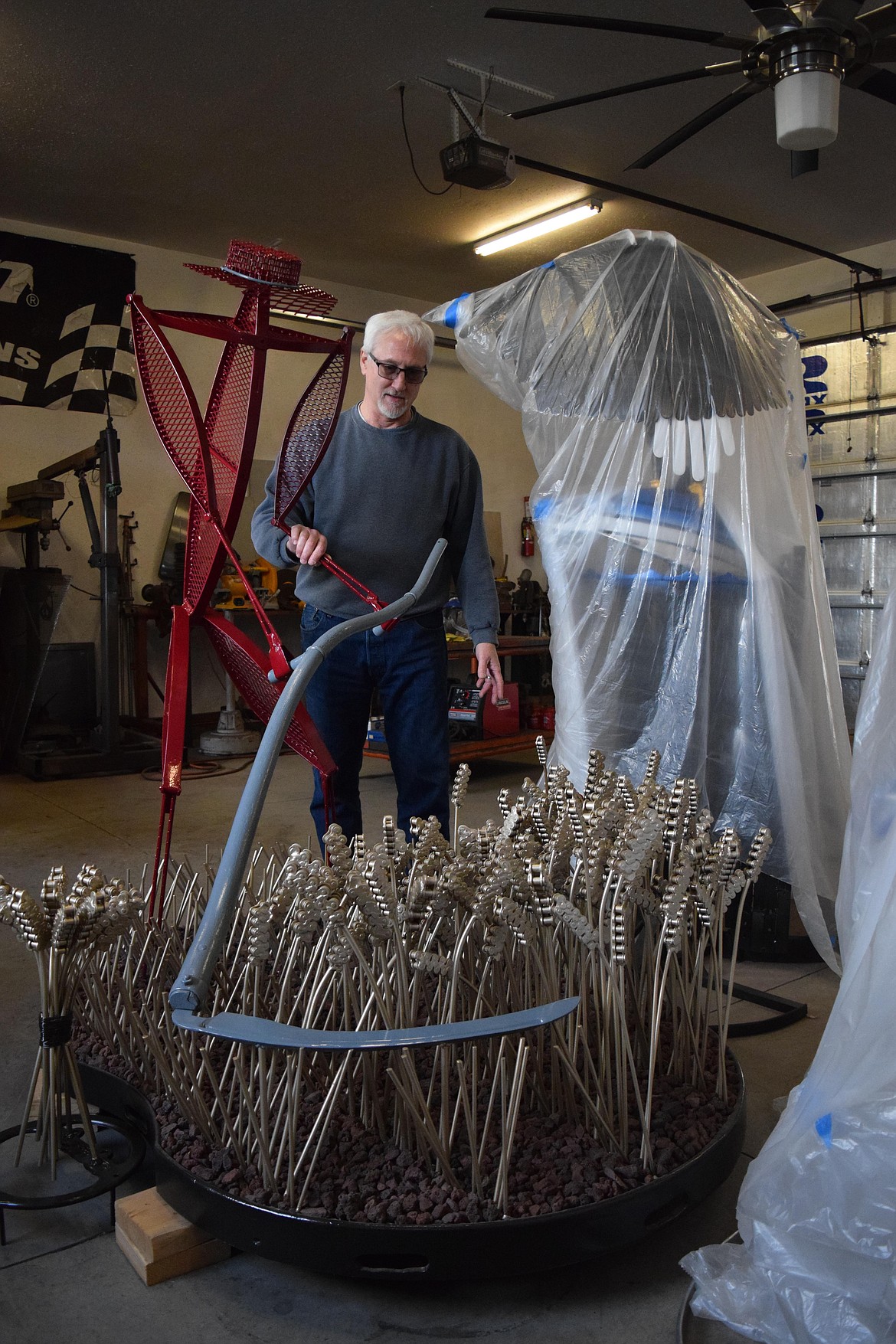Tom Strohmaier shows off the farmer scything wheat sculpture he created from old buggy and combine parts. The work, which is painted in Washington State University’s official crimson, has more than 10,000 individual welds, Strohmaier said.The individual heads of wheat are made from segments of chain taken from old combines.