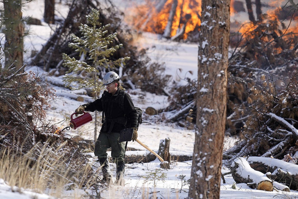 Mile High Youth Corps member John Knudsen set fire to a pile of tree debris alongside U.S. Forest Service firefighters near the Bridge Crossing picnic grounds in Hatch Gulch Wednesday, Feb. 23, 2022, near Deckers, Colo. (AP Photo/David Zalubowski)