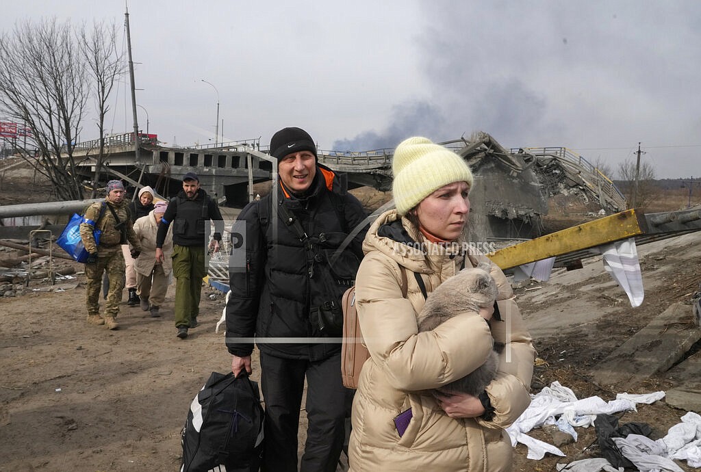 A woman carries her cat near a destroyed bridge as she flees from her hometown on the road towards Kyiv, in the town of Irpin, some 25 km (16 miles) northwest of Kyiv, Saturday, March 12, 2022. Kyiv northwest suburbs such as Irpin and Bucha have been enduring Russian shellfire and bombardments for over a week prompting residents to leave their home. (AP Photo/Efrem Lukatsky)