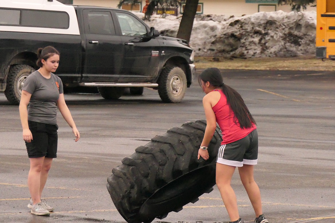 Marsha Klaus (red shirt) flips a large tractor tire to teammate Sacha Fisher during conditioning drills last week at Noxon High.  (Chuck Bandel/Valley Press)