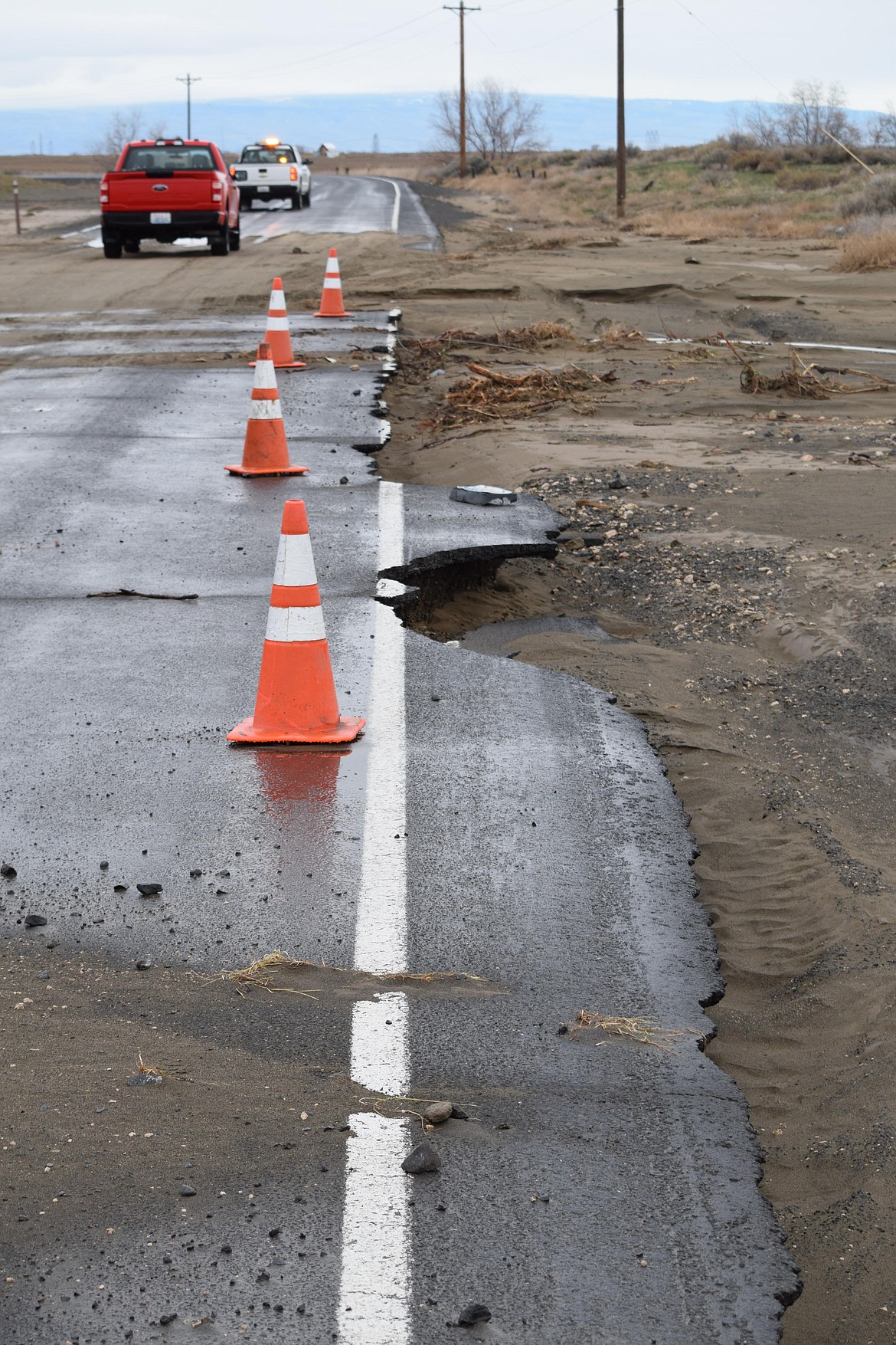 Work crews from the Grant County Public Utility District drive past Monday morning a north shoulder of Frenchman Hills Road W eroded and partially collapsed by a flood caused when a Quincy Columbia Basin Irrigation District canal failed early Friday.