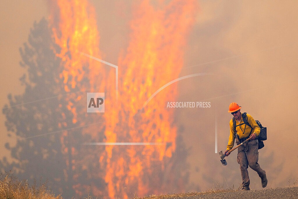 After walking down a gravel road to do recon on a fire cresting into the trees, a wildland firefighter grimaces as he walks back to his crew at the Bedrock Fire north of Lenore, Idaho on Aug. 12, 2021. Idaho Gov. Brad Little has signed into law legislation giving the state's wildland firefighters hazard pay. The Republican governor on Thursday, March 24, 2022, signed the measure that provides state-employed wildland firefighters with hazard pay of up to 25% above their hourly wages. (Pete Caster/Lewiston Tribune via AP, File)