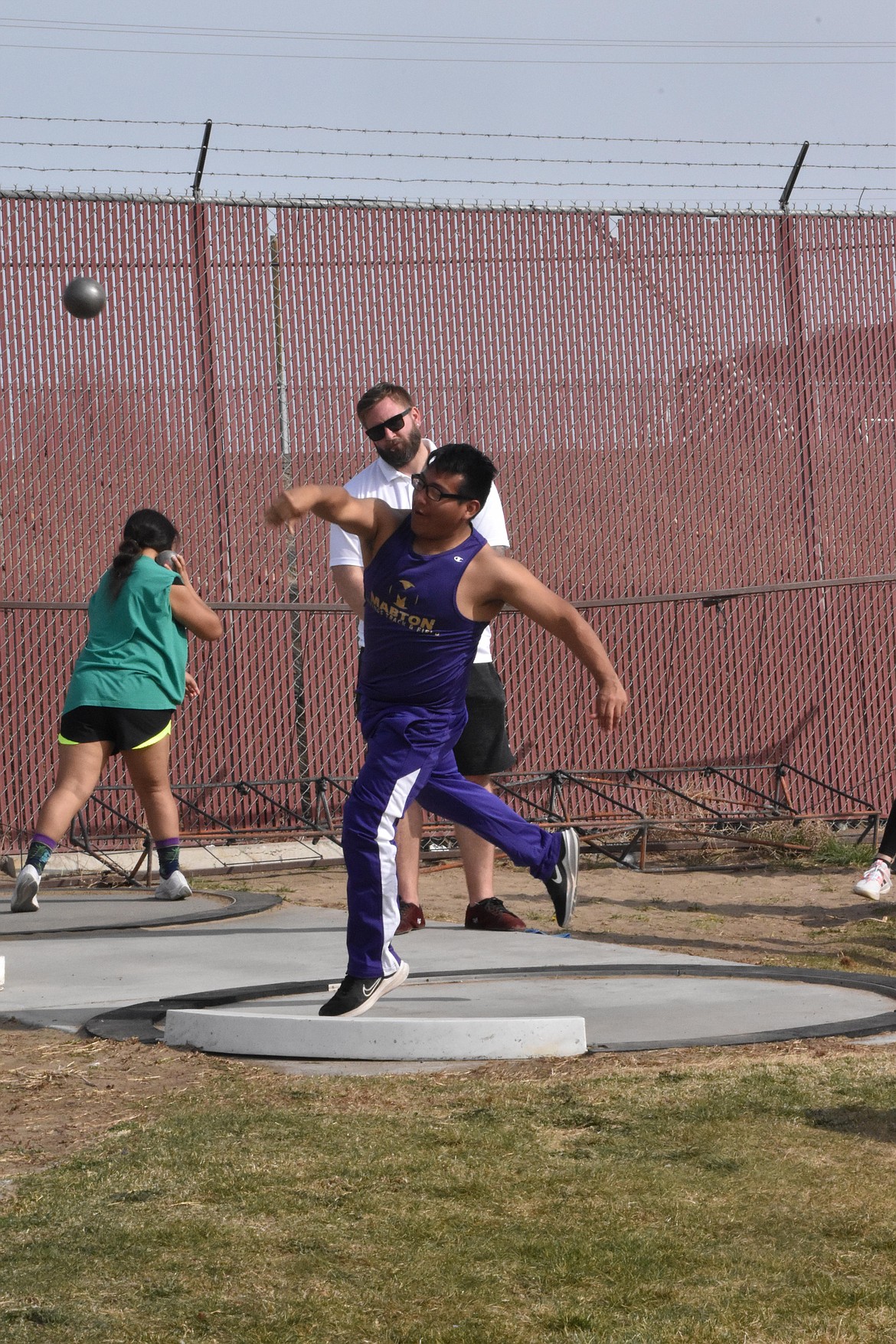 A Mabton High School shot putter practices as national discus champion Jared Schuurmans observes.