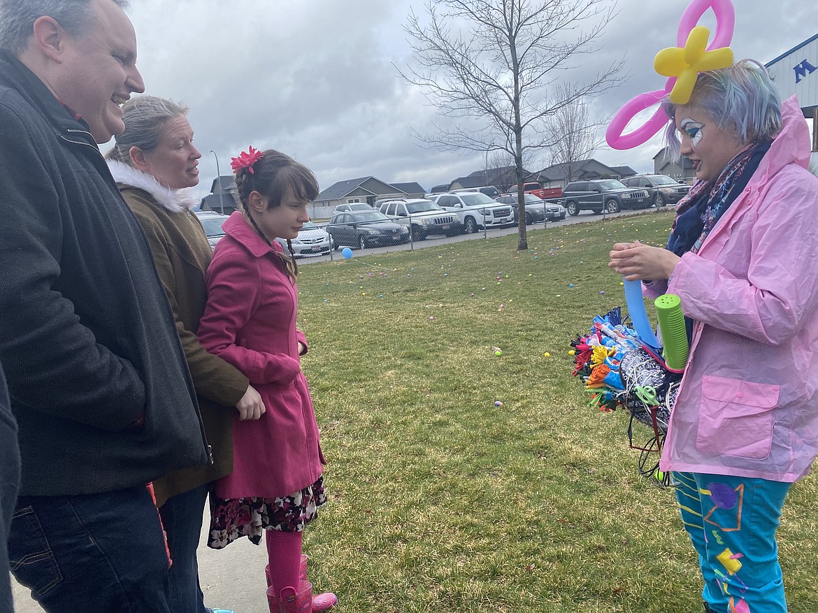 From left: James and Krista Brookes wait with ten-year-old daughter Lily, while Vastra the Clown creates a tied balloon dolphin, at the second annual inclusive Easter egg hunt, Saturday at Majestic Park in Rathdrum.