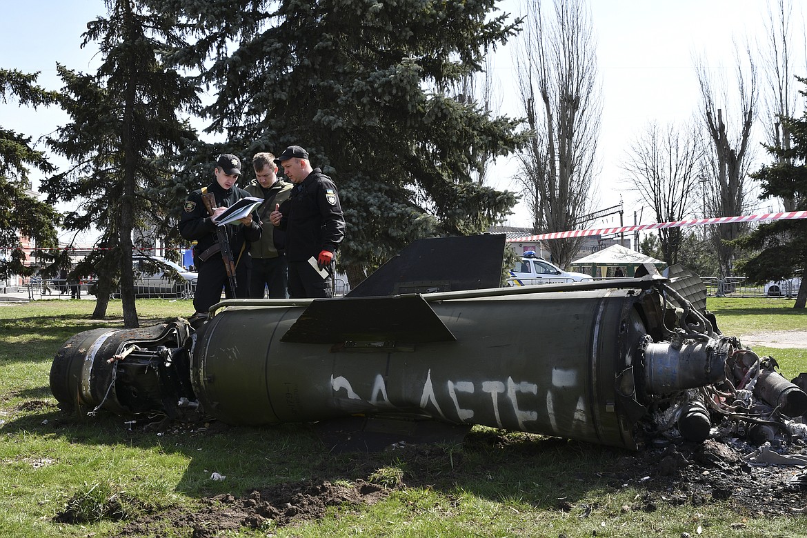 Ukrainian servicemen stand next to a fragment of a Tochka-U missile with a writing in Russian "For children" , on a grass after Russian shelling at the railway station in Kramatorsk, Ukraine, Friday, April 8, 2022. (AP Photo/Andriy Andriyenko)