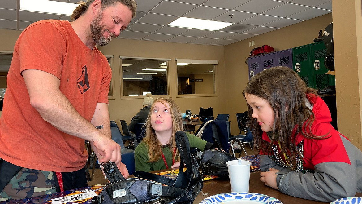 A coach with the Plant a Seed Project assists the kids with their snowboards prior to riding. (Jeff Hawe/Workhat Media)