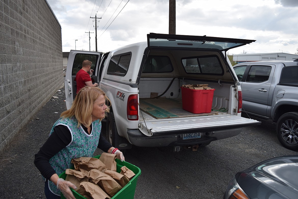 Care Moses Lake volunteer Linda Maw hauls a plastic container of lunch bags ready for delivery late Tuesday.