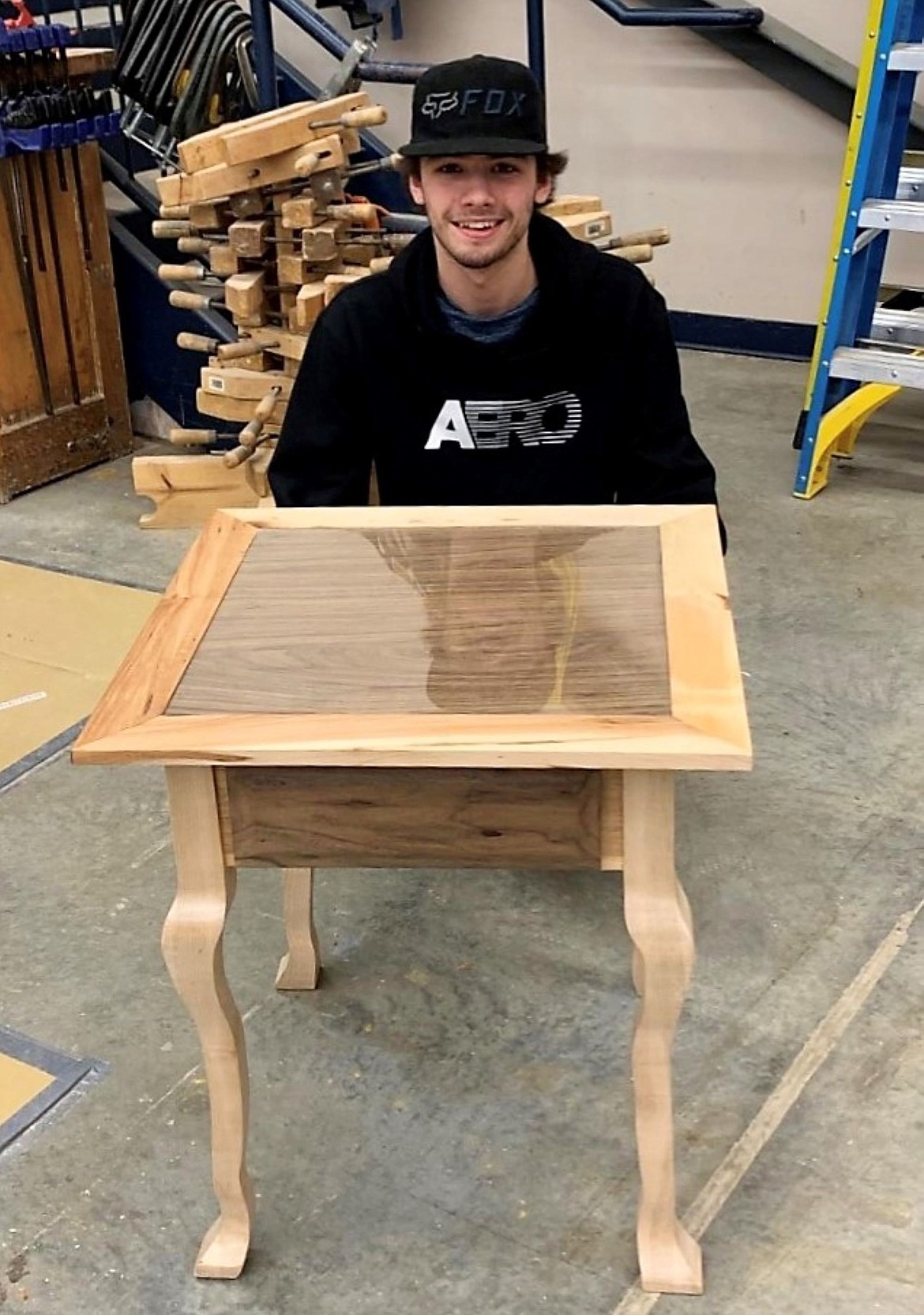 Brady Falck poses with the slim-legged table he created that also features a walnut veneered table top.