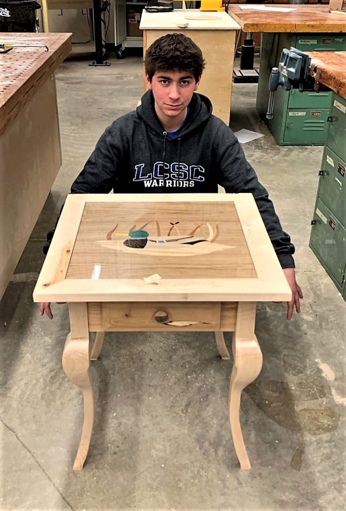 Ryan Carelli poses with his table, which features a variety of natural and dyed woods to create a marquetry duck design on the table top.