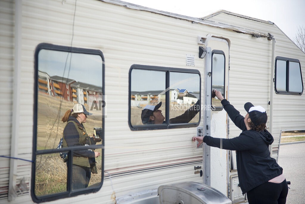 Crystal Baker, a homeless services outreach specialist for the Human Resources Development Council, knocks on the door of a fifth-wheel camper parked behind Kenyon Noble Lumber on Patrick St., in Bozeman, Montana, as her colleague Jenna Huey stands by on Saturday, April 8, 2022. (Samuel Wilson/Bozeman Daily Chronicle via AP)