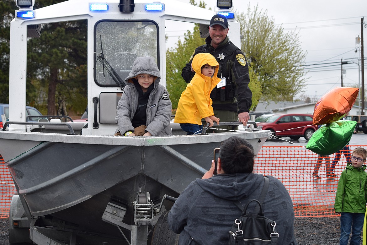 Audrey Surface (foreground) takes a photo of her sons William (gray coat) and Oliver (yellow jacket) and Grant County Sheriff’s Office Maritime Deputy Chris McClanahan at the Moms of Preschoolers Touch-A-Truck fundraiser at Moses Lake Presbyterian Church on Saturday.