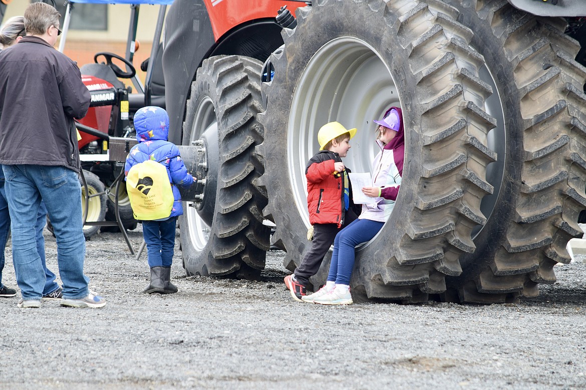 Abigail Taylor (right) sits in the rim of a tractor tire while she talks with her brother Elijah Taylor during the the Moms of Preschoolers Touch-A-Truck fundraiser at Moses Lake Presbyterian Church on Saturday. Abigail described the tractor as “pretty cool” and said climbing up into the cab and looking down made her feel like a giant.