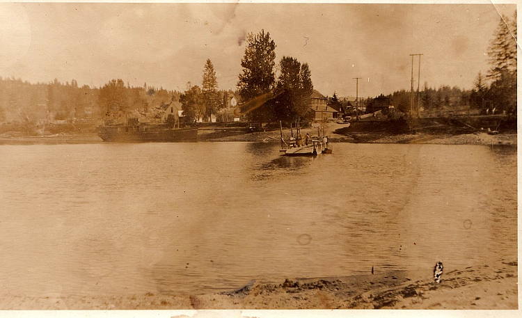 View of Holt Ferry on Flathead River, looking east.  Holt Saloon and Dance Hall visible to left of road on far side of river.  Date unknown--estimated to be around 1900 to 1910. (Whitney Family Collection)