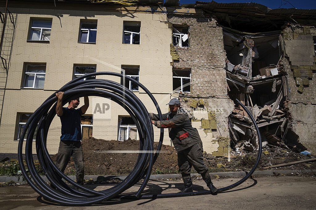 Municipal workers prepare a new tube to restore water supply in front of the building damaged by a Russian attack in Bahmut, Ukraine, on Thursday, May 12, 2022. (AP Photo/Evgeniy Maloletka)