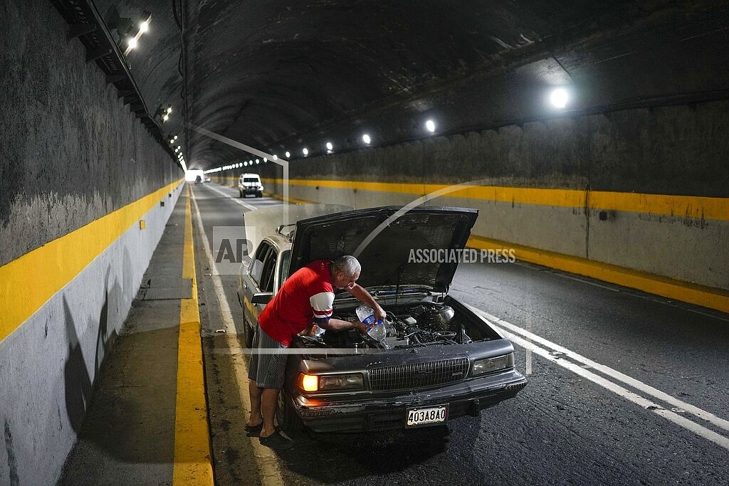 A man tries to cool down his overheating car by pouring water into the radiator, in one of the tunnels of the road that connects La Guaira with Caracas, Venezuela, Tuesday, April 19, 2022. Drivers try to coax a little more life out of aging vehicles in a country whose new car market collapsed and where few can afford to trade up for a better used one. (AP Photo/Matias Delacroix)