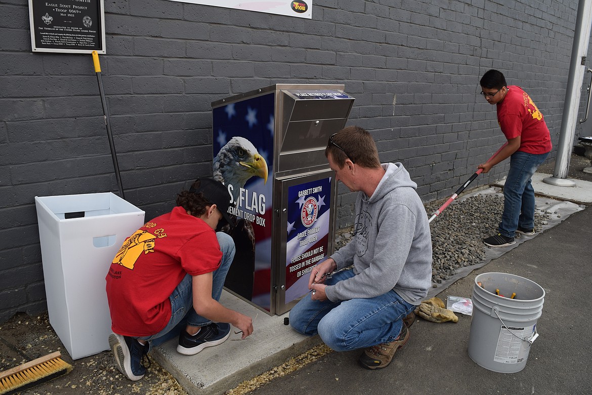 Boy Scouts of America Troop 0069 Assistant Scout Leader Mike Helvy (center) works with Boy Scout Thomas Howard to secure the new dropbox for old and worn-out American flags while Francisco Campos rakes gravel in the parking lot of American Legion Joe R. Hooper Post 209 in Moses Lake on Thursday.