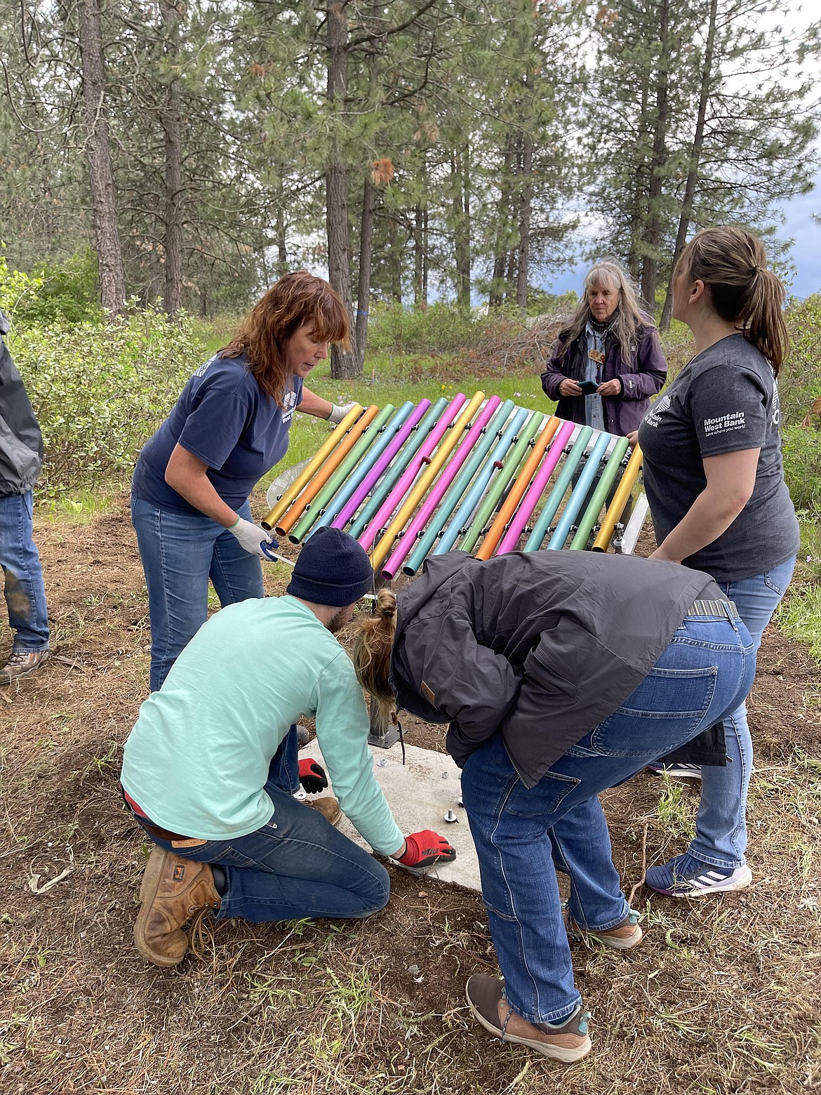 Volunteers in a circle from far left: Teri Grenne, with Mountain West Bank, Jordan Bader with Coeur d'Alene Gizmo, Lauren Bokman, with Gizmo, Stephanie Todd, with Mountain West and Janine Bokman, with Gizmo collaborate on the installation of a colorful xylophone at Children's Village sensory park, Friday.