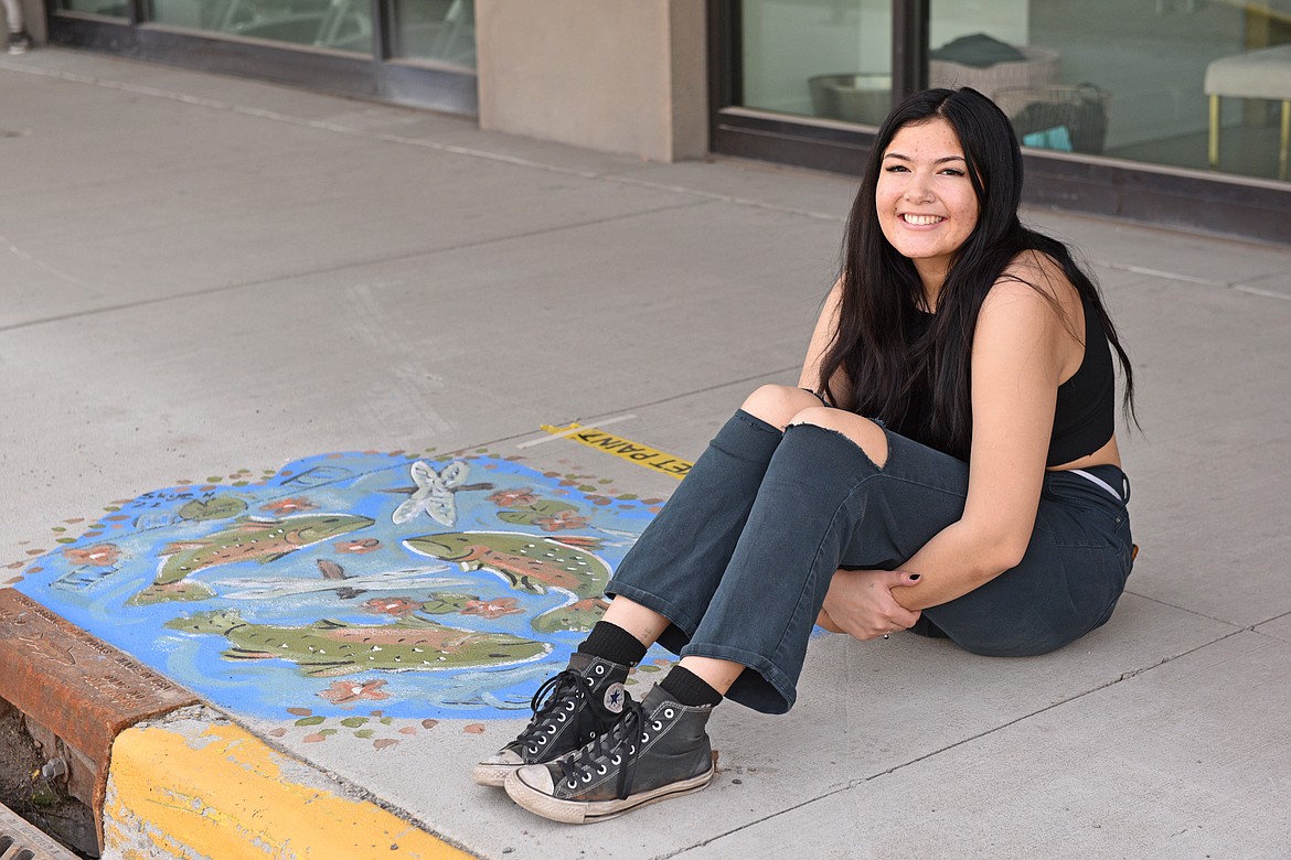 Whitefish High School's Advanced Art student Skye Horowitz sits beside her mural on a downtown storm drain. (Julie Engler/Whitefish Pilot)