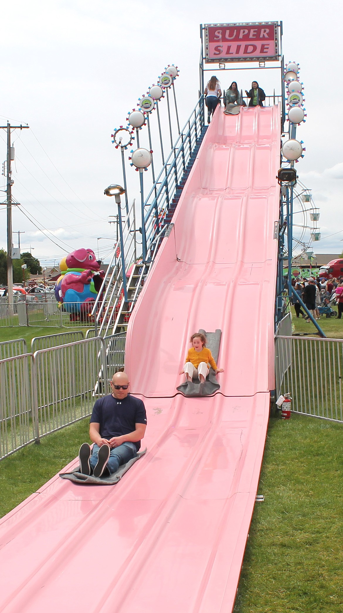 Sam Rathbone, left, and 5-year-old Ila Rathbone swoop down the Super Slide at the Moses Lake Spring Festival Saturday. The carnival was crowded after two years without a festival.