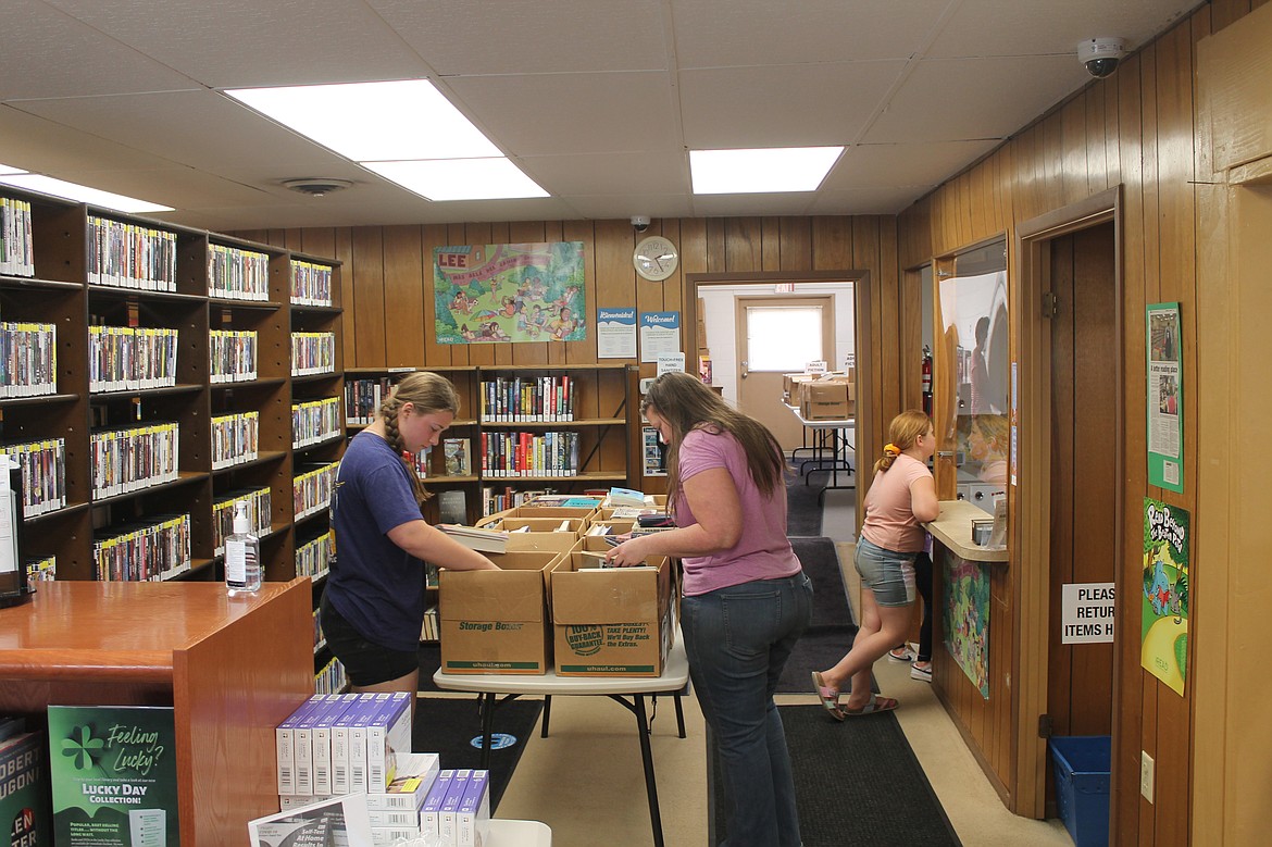 Eleanor Millage, left, and Erin Morse browse through boxes of books at the Warden Library book sale, while 9-year-old Maggie Morse chats with librarian Jean Russell. The Morse family homeschools, and Erin said she found some good books for lessons.