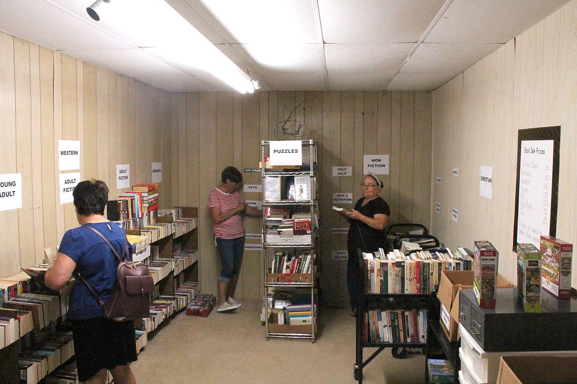 Paula Martinez, left, and Rosie Martinez, right, browse through books while Friends of the Library volunteer Vicki Underhill arranges the shelves. The Warden Library held its book sale Thursday.