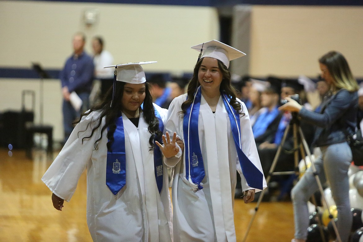 Two graduates link arms and wave to families upon walking to their seating for the graduation ceremony at Soap Lake High School.