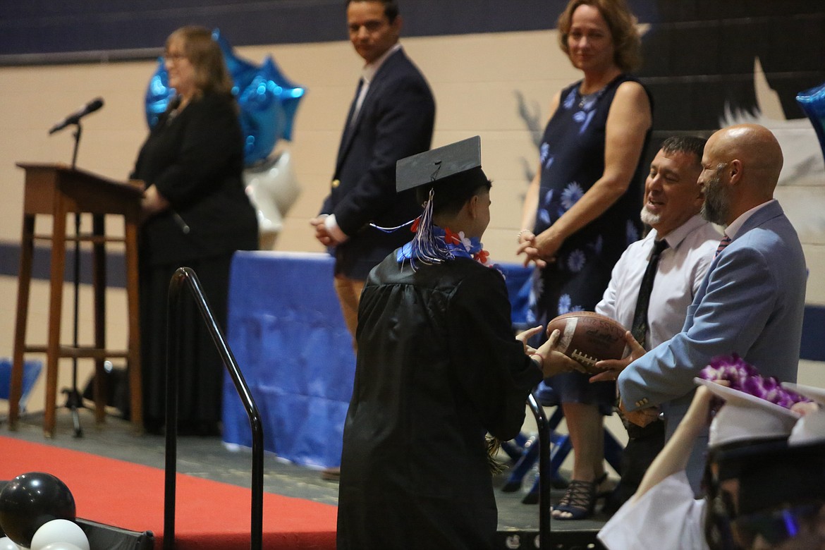 Soap Lake’s Christian Foster (left) runs up to the side of the graduation stage to give a football to his coach, Tony Blankenship (right center).