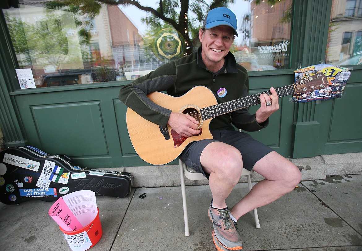 Dr. Ben Perschau smiles as he plays acoustic guitar on Sherman Avenue on the first day of Street Music Week. He was happy to participate, despite the pouring rain.