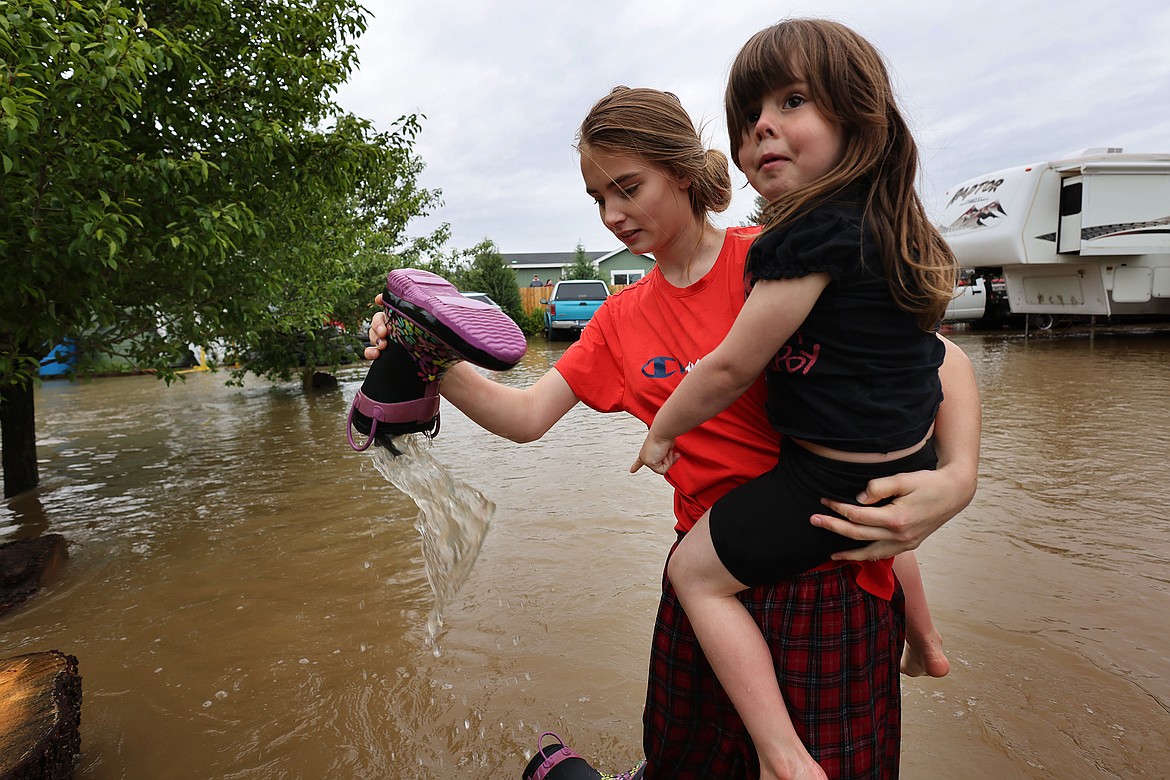 Jordan Stanley dumps the water from Ellie Henderson's boots after wading through the flood waters near their home in Columbia Falls Wednesday, June 15. (Jeremy Weber/Daily Inter Lake)