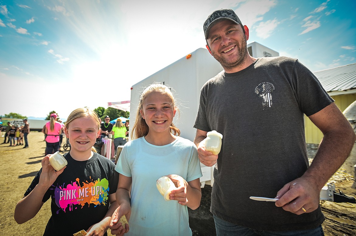 Jon Woods and his daughters Charlotte, left, and Hannah shake their jars of heavy whipping cream to make butter at Kalispell Kreamery's Milk & Cookies event on Saturday, June 18. (Casey Kreider/Daily Inter Lake)