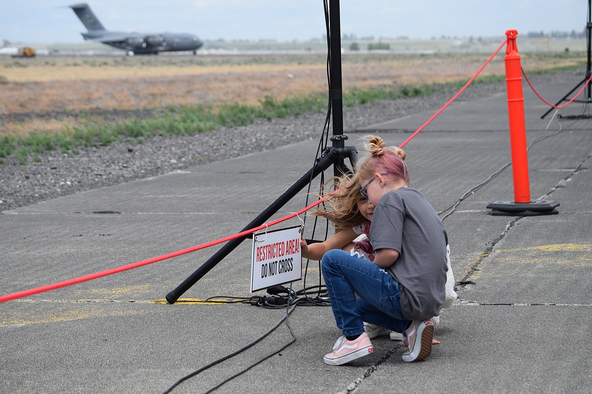 A pair of girls kneel near the edge of the viewing area on the 10,000-foot-long secondary runway at the Grant County International Airport as an Air Force C-17 transport lands following its performance flight at the Moses Lake Airshow on Saturday.