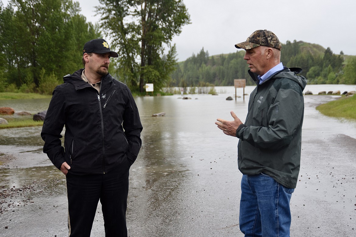 Flathead County Sheriff Brian Heino, left, updates Gov. Greg Gianforte on flooding in Northwest Montana during a briefing Monday, June 20 at the Old Steel Bridge fishing access on the Flathead River in Evergreen. (Matt Baldwin/Daily Inter Lake)