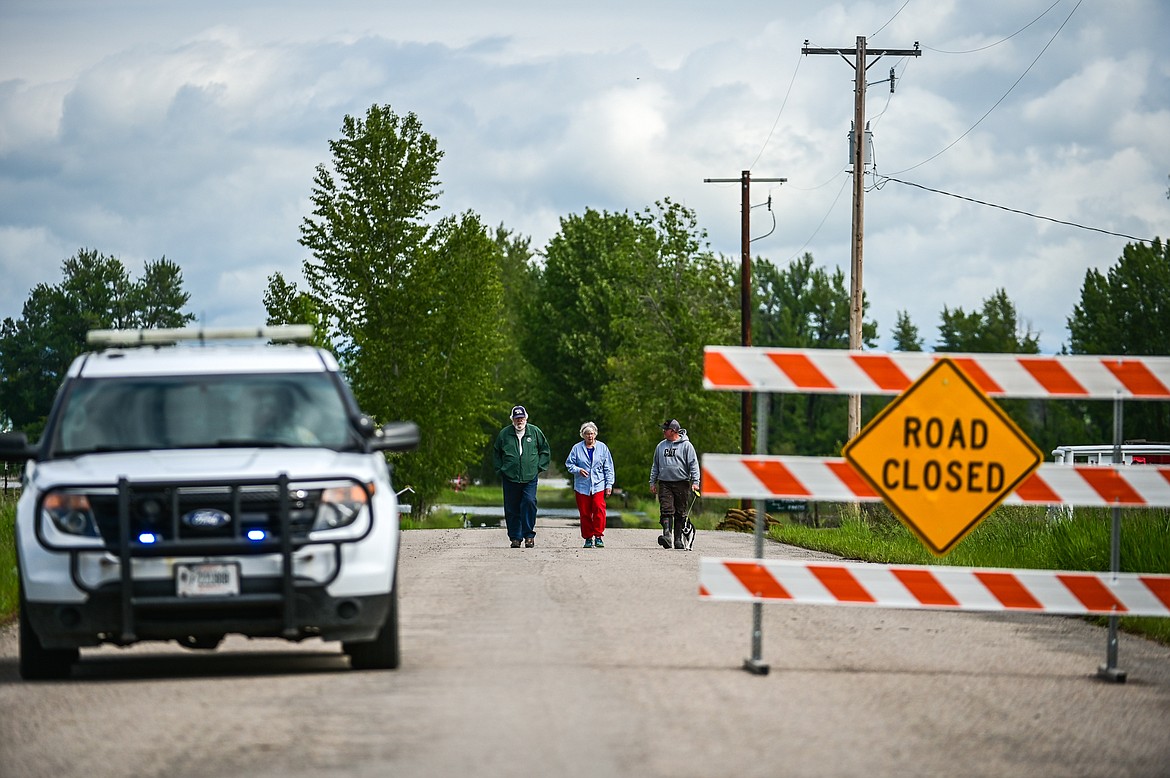 Residents of Wagner Lane walk along the roadway surveying flooding from the Flathead River behind a roadblock set up by the Flathead County Sheriff’s Office on Tuesday, June 21. (Casey Kreider/Daily Inter Lake)