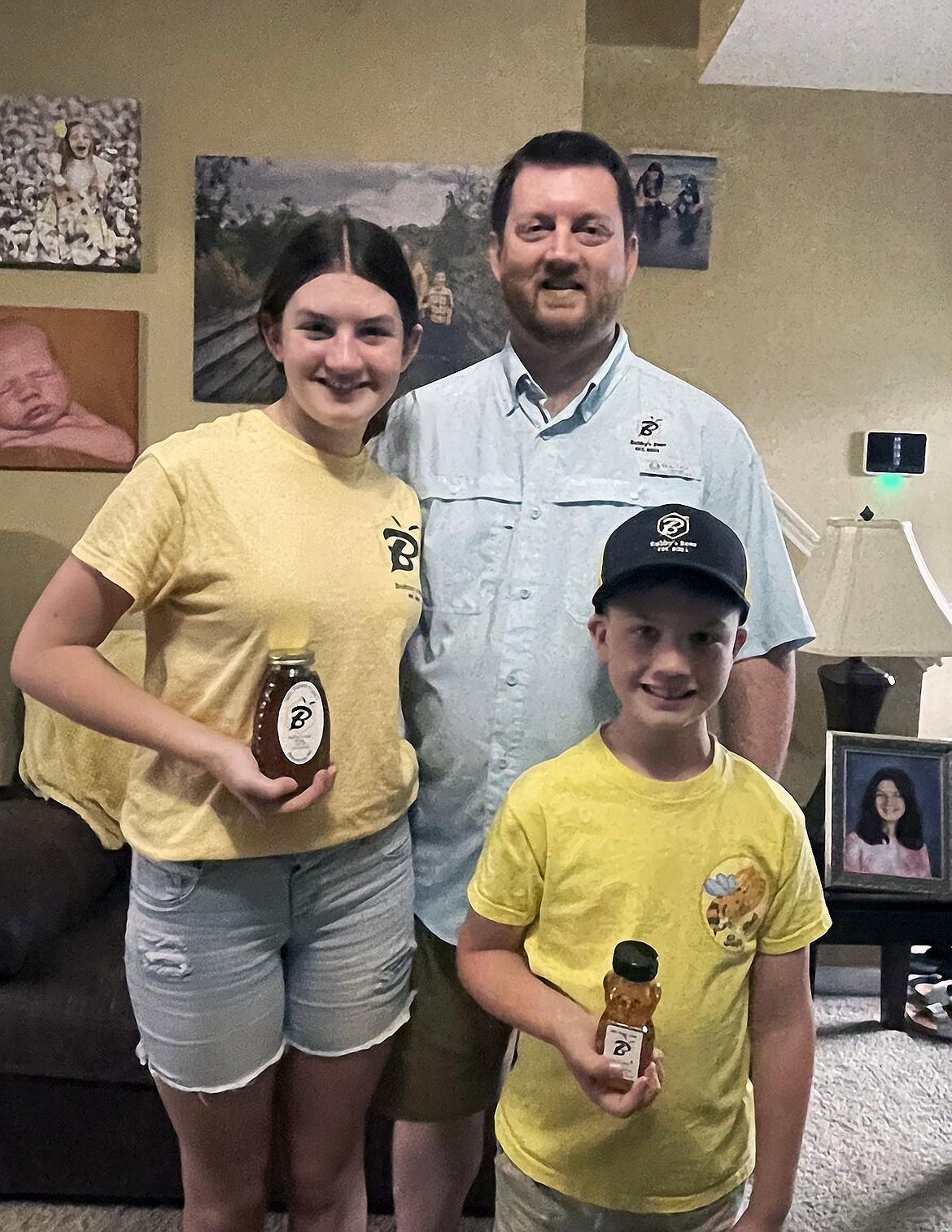 Taylor, left, Carter, right, and dad Randall Jones, center, smile in their Bubby's Bees merchandise, Monday, June 13, 2022 in Jacksonville, N.C. What started as making honey for their four-person family, turned into a successful startup called Bubby's Bees, one that all four members of the Jones family have played a part in. (Morgan Starling/The Daily News via AP)