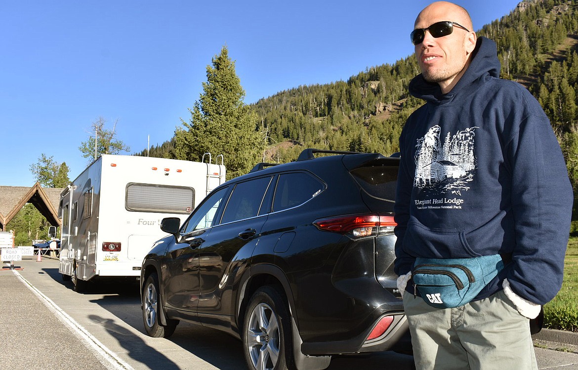 Muris Demirovic waits by his rental car outside Yellowstone National Park for the entrance gate to open, Wednesday June 22, 2022, near Wapiti, Wyo. Demirovic said he was supposed to leave the area earlier in the week but extended his trip to get in the park when it partially reopened after flood damage forced it to close last week. (AP Photo/Matthew Brown)