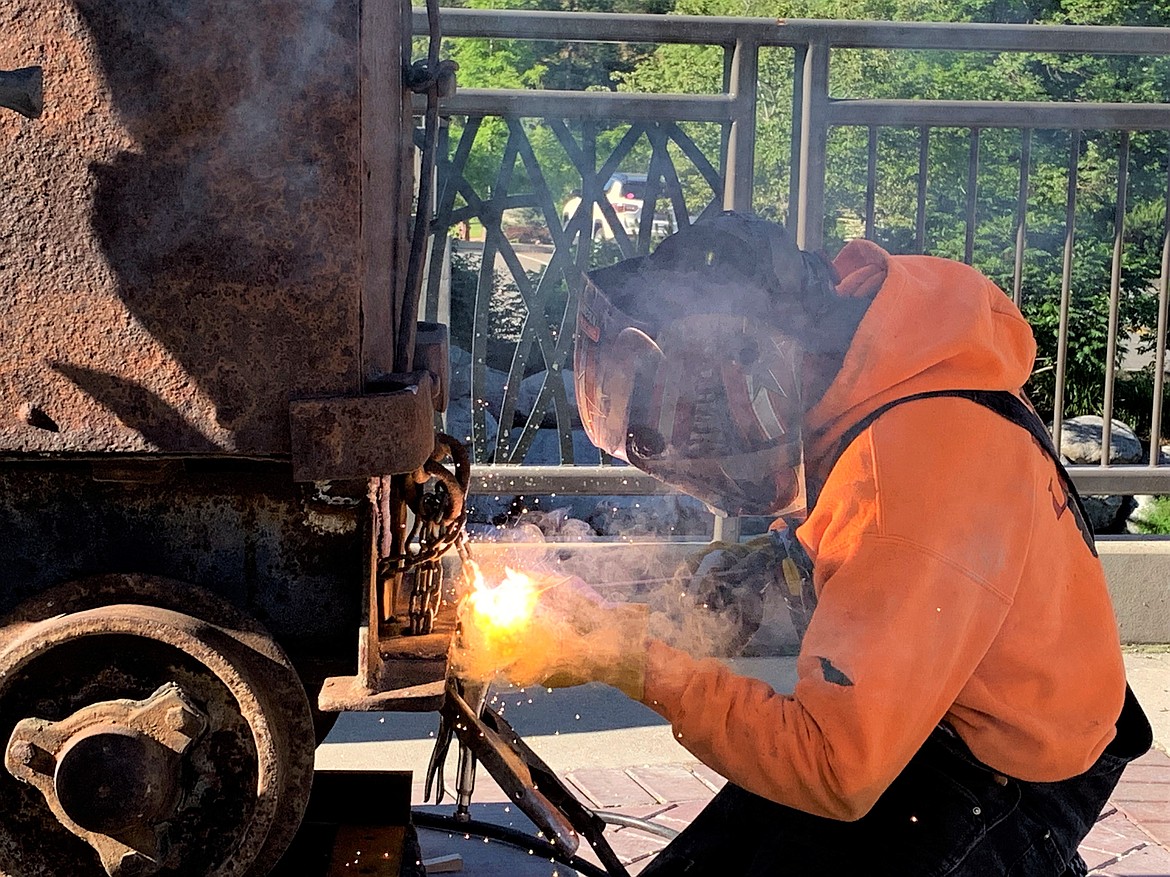John Wallace of Allied Weldery, Inc. welds a chain on the ore cart with The Miner statue on Wednesday.