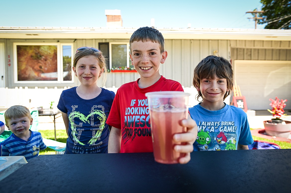 Jessi, Ethan and Jonathan Mathison serve up a cup of their cherry lemonade as their younger brother Sawyer, bottom left, watches at their Galactic Lemonade/Captain Fizzy's Limonade stand as part of Lemonade Day in Kalispell on Saturday, June 25. The national Lemonade Day program helps youth learn about starting a business, via the one-day stands. Through guided lessons in their Lemonade Day booklet, they learn about budgeting, finance, site selection, product creation, supplies, staffing, and more. (Casey Kreider/Daily Inter Lake)