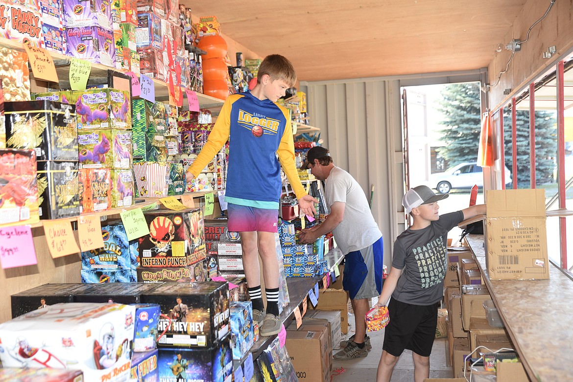 Noah Scofield hands fireworks to Hudson Hannah while Kyle Hannah stacks merchandise on Tuesday at the Black Raptor fireworks stand in Libby in preparation for the upcoming July 4 holiday, recognizing our nation's 222nd year of independence. (Scott Shindledecker/The Western News)